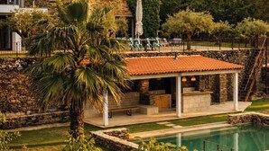 A stone house with a pool, outdoor seating, and a staircase leading to a balcony.