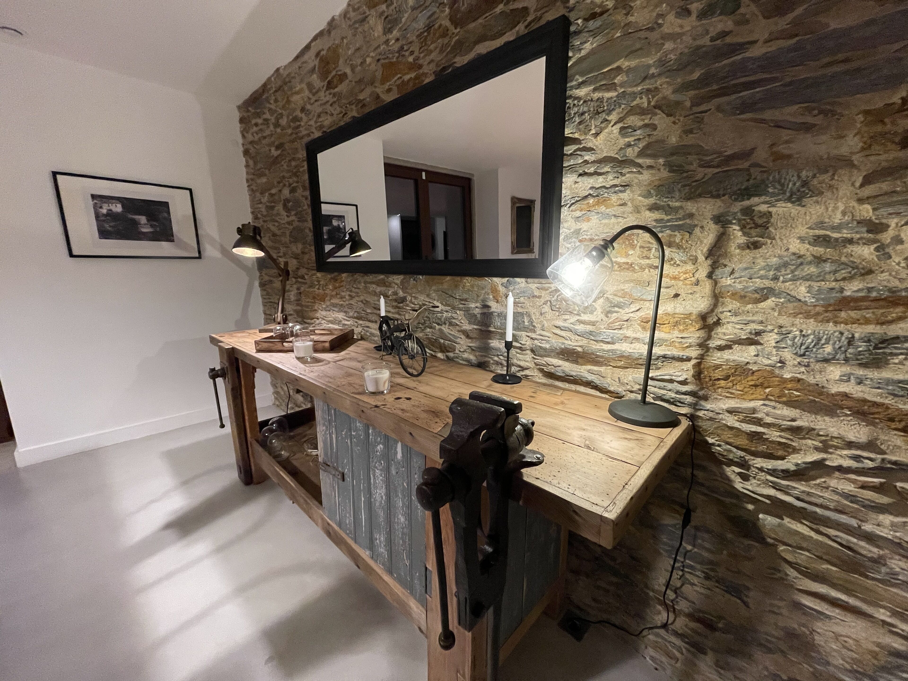 A bathroom with a stone wall, a wooden vanity, a mirror, a sink, a bicycle, and a lamp.
