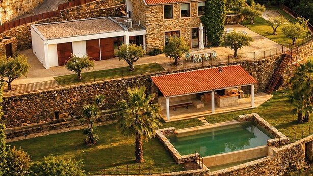 A stone house with a red-tiled roof, a swimming pool, and a stone wall.