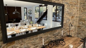 A dining area with a large mirror reflecting the room, a stone wall, a wooden table set for dining, and a vintage motorcycle.