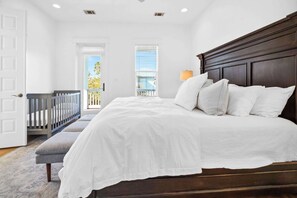 A bedroom with a large bed, a grey bench, a white door, and a window with blinds. - Golf Cart｜4bed, 3.5 bath｜Luxury 30A Getaway! (Santa Rosa Beach)