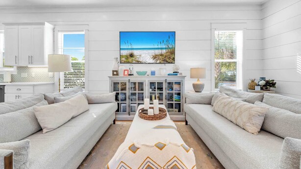 A modern living room with a central coffee table, two sofas, a cabinet with decorative items, and a beach-themed painting on the wall. - Golf Cart｜4bed, 3.5 bath｜Luxury 30A Getaway! (Santa Rosa Beach)