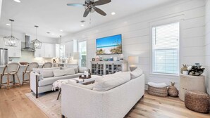 A spacious living area with a large gray sectional sofa, a dining area with wicker chairs, and a kitchen with white cabinets. - Golf Cart｜4bed, 3.5 bath｜Luxury 30A Getaway! (Santa Rosa Beach)