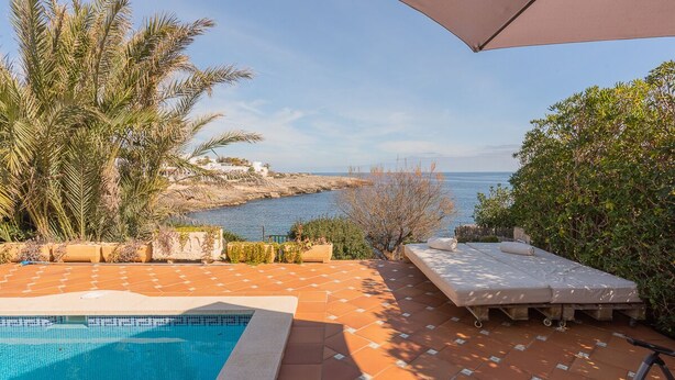 Un espace piscine avec vue sur la mer, un coin salon avec un matelas et des coussins, et un grand parasol.