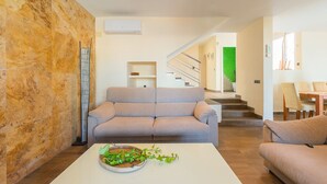 Un salon moderne avec un canapé beige, une table basse blanche agrémentée d’une plante, et un escalier menant à un espace éclairé de lumière verte.