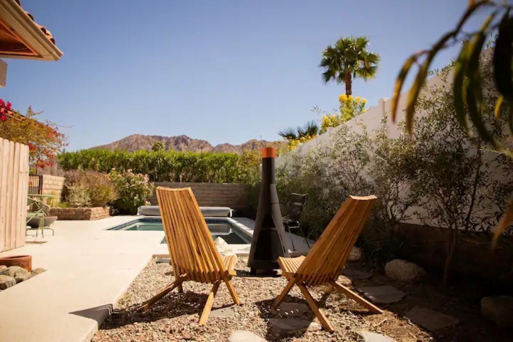 Une terrasse avec deux chaises en bois, un barbecue et une piscine.