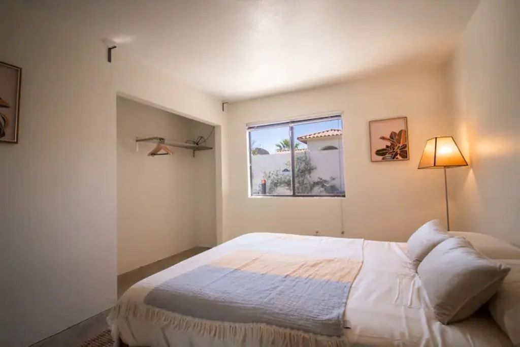 A bedroom with a bed, a window, a wall-mounted lamp, and a framed picture.