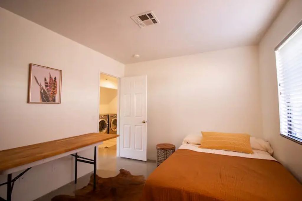 A bedroom with a bed, a bench, a door, and a small round table.