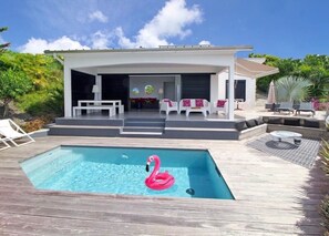 Een modern huis met een zwembad, terras en een tropische tuin.