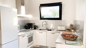 Une cuisine moderne avec des armoires blanches, un four encastré, un four à micro-ondes, une machine à café et une fenêtre au-dessus de l’évier.