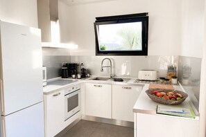 Een moderne keuken met witte kastjes, een inbouwoven, een magnetron, een koffiezetapparaat en een raam boven de gootsteen.