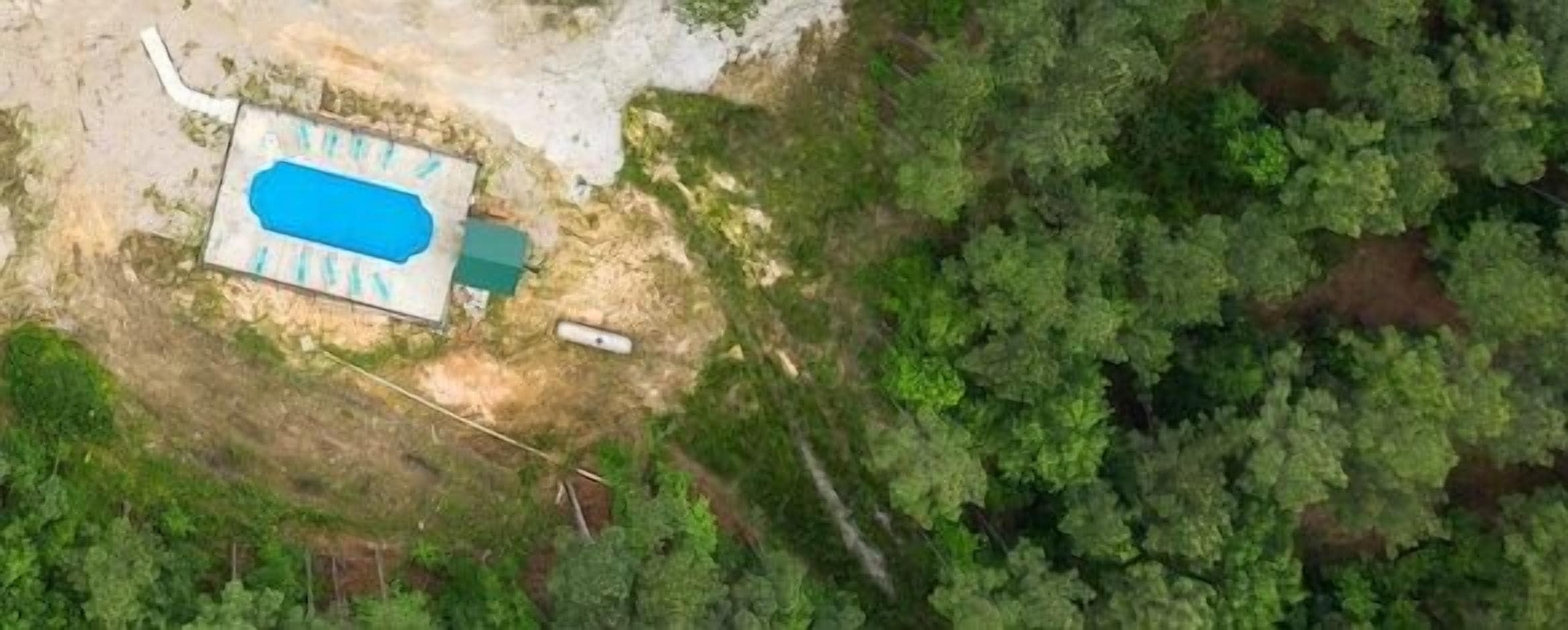 Vista aérea de una propiedad con piscina, rodeada de bosque denso.