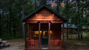 A log cabin with a porch, a sign reading "Red River", and a gravel path leading to it. - Beautiful cabins with a pool in a peaceful setting (Broken Bow)