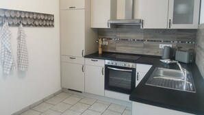 A modern kitchen with white cabinets, a black countertop, an oven, a sink, and a backsplash with a wood-like pattern. - Schwarzwaldmarie Ferienwohnung (löffingen)