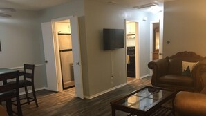 A living room with a glass coffee table, a brown leather sofa, and a dining area with a table and chairs. - Cozy Modern 1 Bed 1 Bath next to Park! (Van)