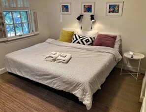 A neatly made bed with a patterned bedspread and two folded towels. There are three pillows in various colors and patterns. A small round table with a picture frame is beside the bed. - Quiet Street by Georgetown & GWU, Free Parking + EV Charger (Washington)