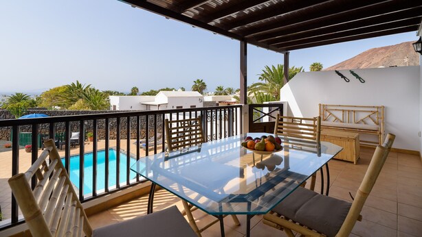 Une table avec un plateau en verre, des chaises et un saladier rempli de fruits, une piscine et une vue sur le paysage.