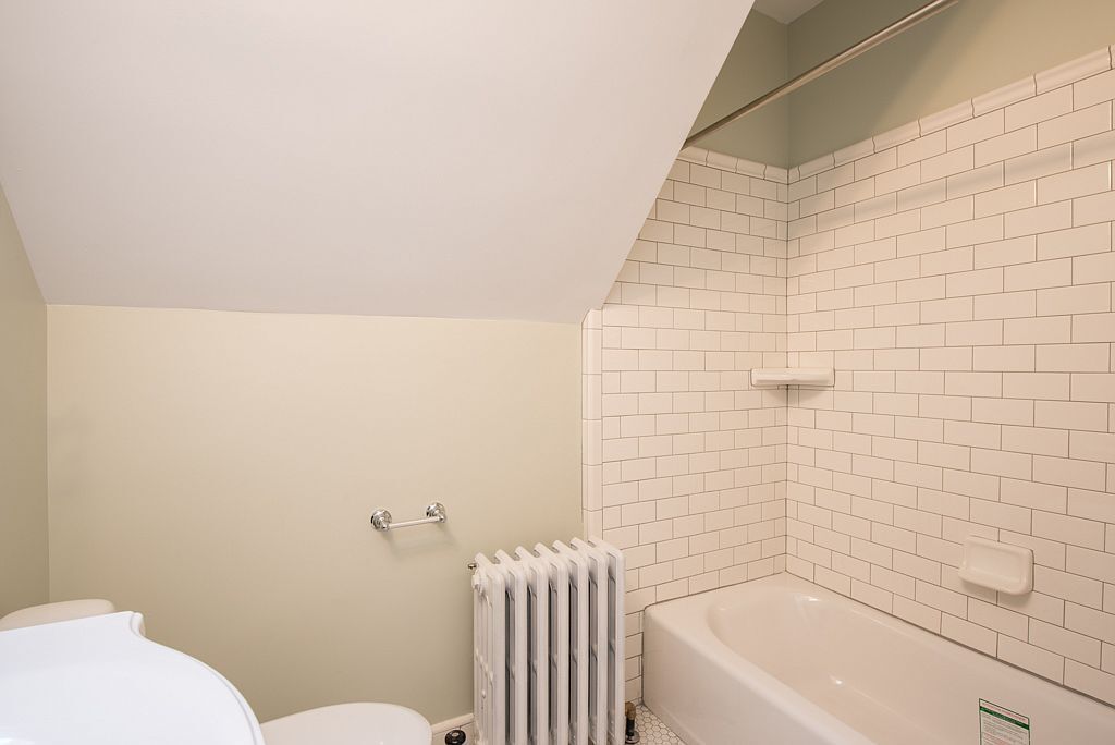 A bathroom with a toilet, a radiator, and a bathtub.