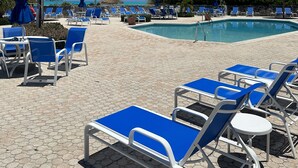 A poolside area with blue lounge chairs and umbrellas, a clear blue sky, and a flag. - Escape to the Beach (Treasure Cay, North Abaco)