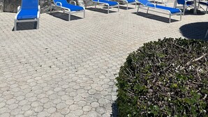 A beachside lounge area with blue lounge chairs, a thatched umbrella, and a flag. - Escape to the Beach (Treasure Cay, North Abaco)