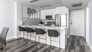 A modern kitchen with a central island, bar stools, stainless steel appliances, and a patterned backsplash. - 2BR 2BA AMAZING NEWLY RENO BEACHFRONT APT W/BEACH VIEW (Hollywood)