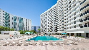 A pool area with lounge chairs and a clear blue pool, surrounded by high-rise buildings. - 2BR 2BA AMAZING NEWLY RENO BEACHFRONT APT W/BEACH VIEW (Hollywood)