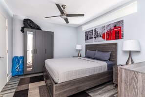 Un dormitorio con cama, mesitas de noche, ventilador de techo, armario y un cuadro en la pared.