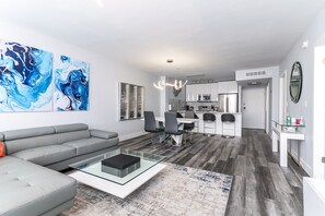A modern living room with a grey sofa, a glass coffee table, and abstract art on the wall.