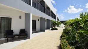 A modern hotel with a covered outdoor seating area, a tiled walkway, and lush greenery. - Wayaca CondoArena at Eagle Beach (Oranjestad-west)