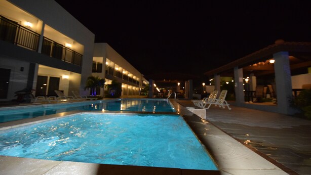 A swimming pool area with lounge chairs and a building with balconies. - Wayaca CondoArena at Eagle Beach (Oranjestad-west)