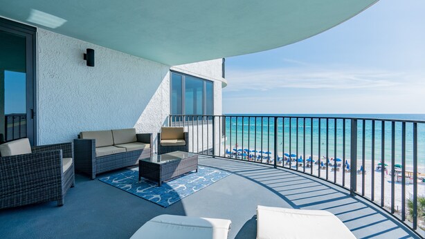 Un balcón con mobiliario de mimbre, una mesa de vidrio y vistas a la playa y al océano.