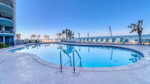 Una piscina con cielo azul despejado, palmeras y un edificio con balcones.