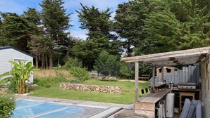 Un jardin avec une piscine, un espace barbecue et un mur en pierre.