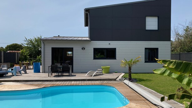 Une maison moderne à deux étages, dotée d’une piscine, de mobilier d’extérieur et d’un petit jardin.