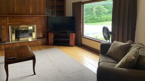 Una sala de estar con chimenea, televisor y un amplio ventanal con cortinas.
