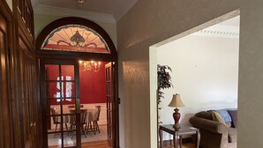 Un pasillo que conduce a un comedor con un ventanal de vitrales, una araña y un suelo de madera.