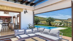 A modern outdoor living area with a sectional sofa, a wooden coffee table, and a pool view.
