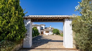 A stone pathway leading to a white building with a tiled roof, surrounded by greenery.