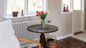 Une pièce avec une table ronde, un panier en osier, un radiateur et une fenêtre donnant sur des arbres.