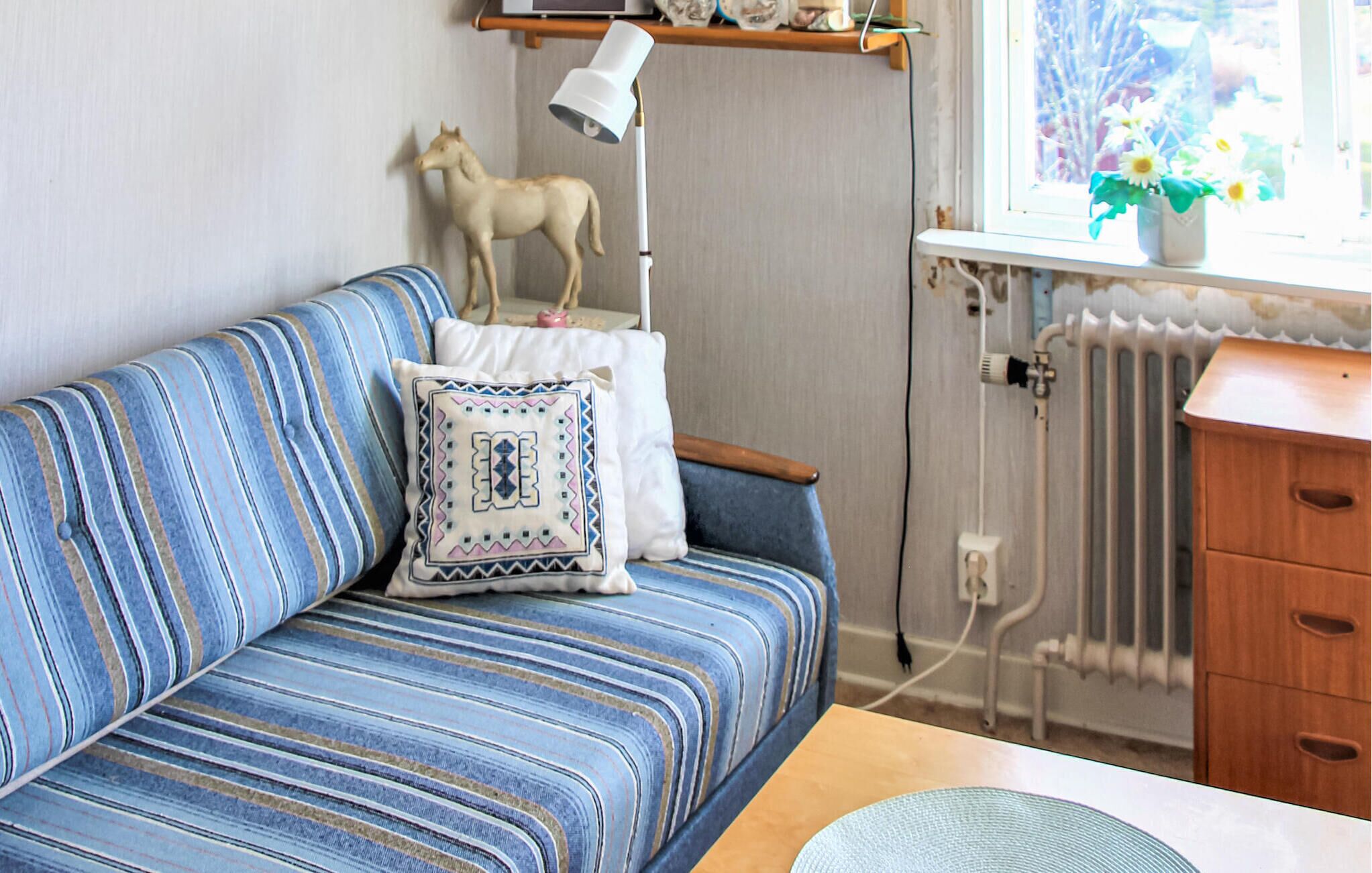 Une pièce avec un canapé bleu à rayures, une lampe blanche, un radiateur et un meuble en bois.
