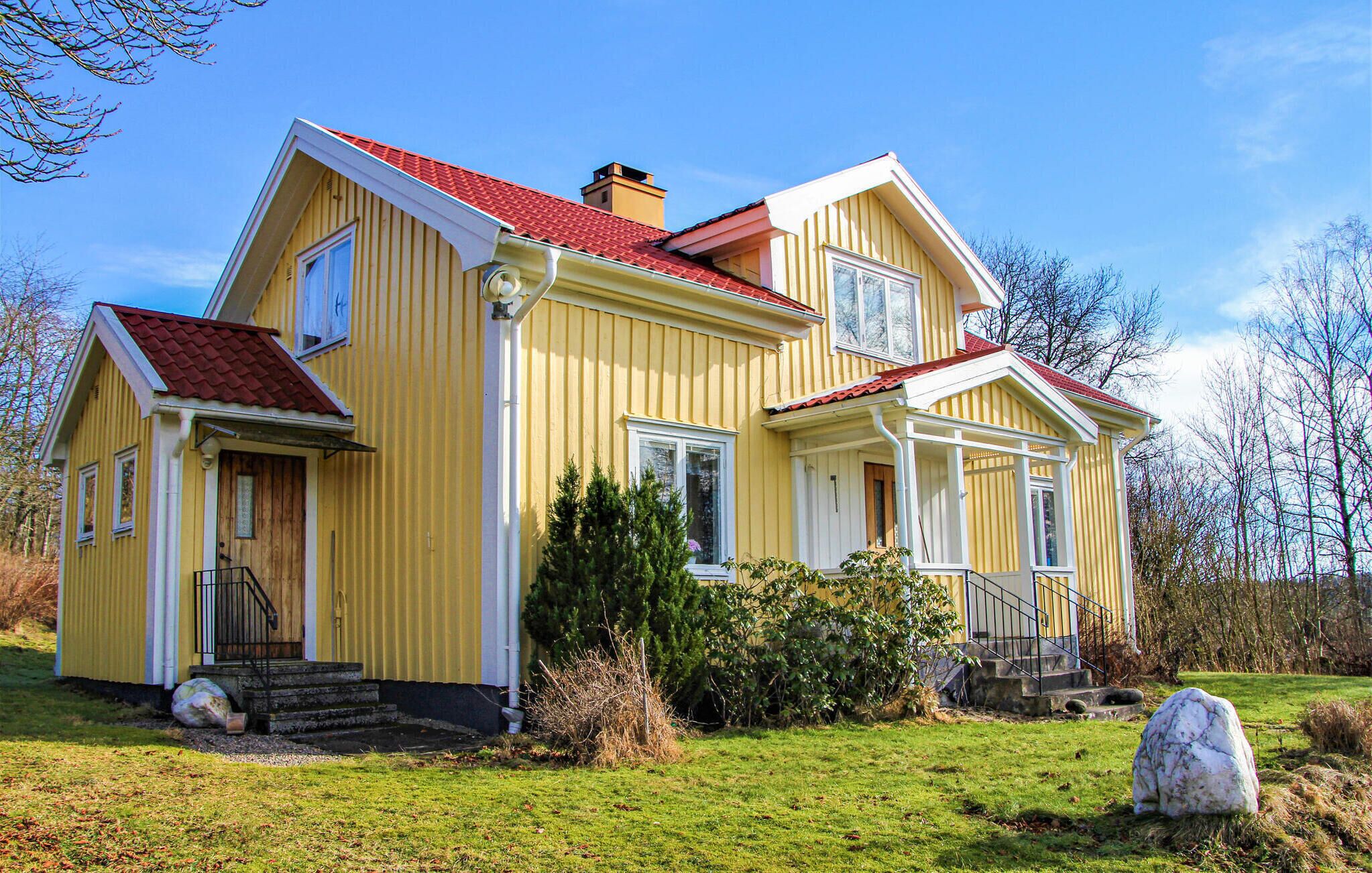 Une maison jaune à deux étages, avec un toit rouge, un porche à l’avant et un petit jardin.