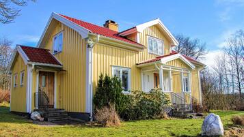 Une maison jaune à deux étages, avec un toit rouge, un porche à l’avant et un petit jardin.