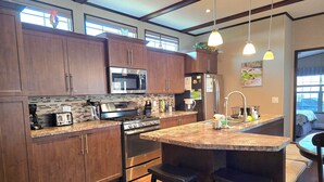 A modern kitchen with wooden cabinets, stainless steel appliances, a large island with stools, and pendant lighting.