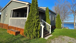 A two-story house with a porch and a small deck, surrounded by greenery and a body of water.