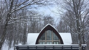 A snow-covered cabin with a large arched window and a wooden deck in front. - Stratton Mountain Home Hot Tub, Fire Pit and walk to the mountain. (Stratton)