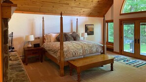 A four-poster bed with a bench, two bedside tables, and a large window with a view of greenery. - Stratton Mountain Home Hot Tub, Fire Pit and walk to the mountain. (Stratton)