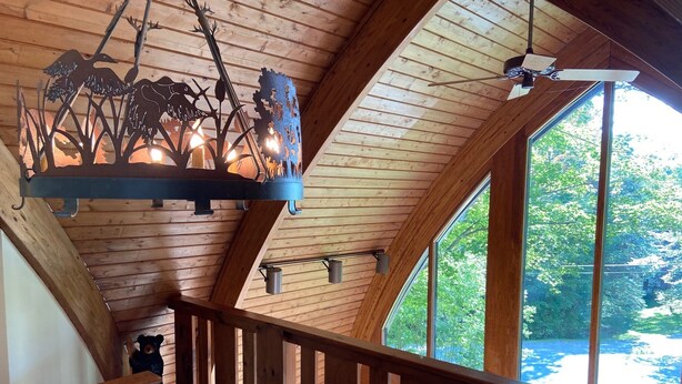 A wooden interior with a staircase, a metal chandelier, and large windows offering a view of the outdoors. - Stratton Mountain Home Hot Tub, Fire Pit and walk to the mountain. (Stratton)