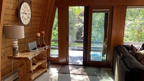 A cozy room with wooden walls, a large window, a wooden desk, a lamp, a clock, and a couch. - Stratton Mountain Home Hot Tub, Fire Pit and walk to the mountain. (Stratton)