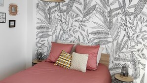 A bedroom with a bed, a hanging lamp, and a wall with a leaf pattern.