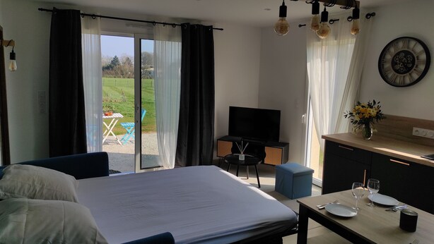 A hotel room with a bed, a TV, a dining table set for two, and a view of the outdoors.